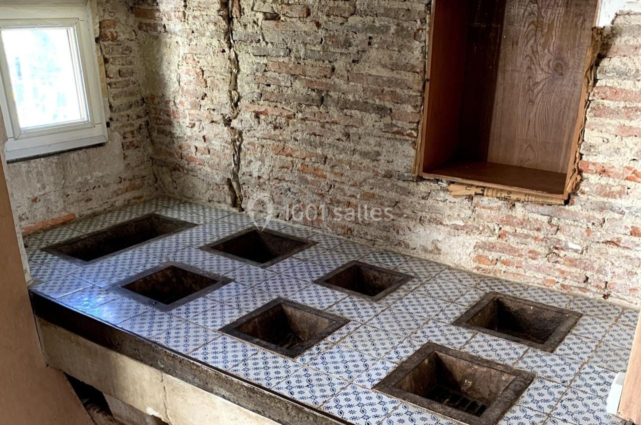 Plan de travail ancien en carreaux de faïence avec plusieurs ouvertures carrées, dans une pièce aux murs en briques.
