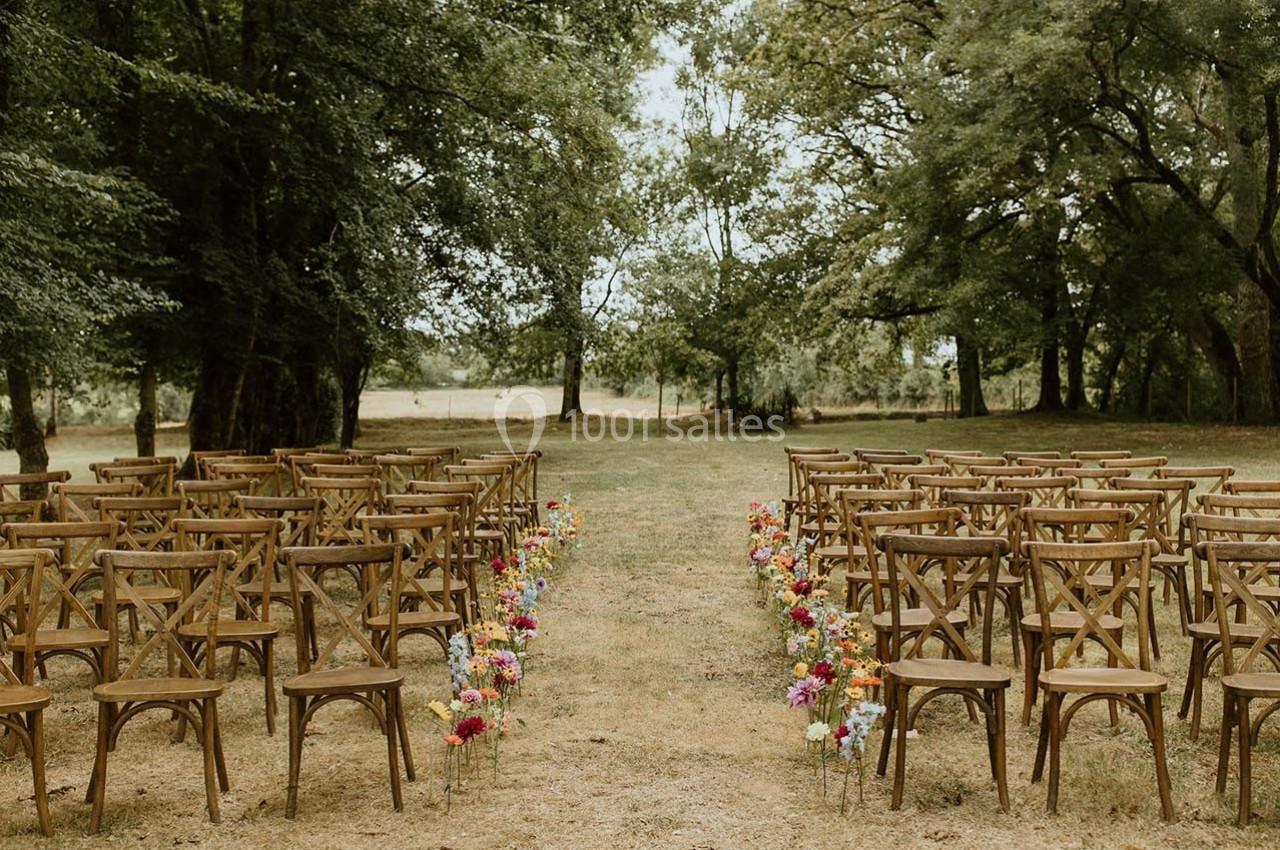 Chaises en bois disposées en rangées sur une pelouse, encadrées de fleurs colorées, dans un cadre arboré.