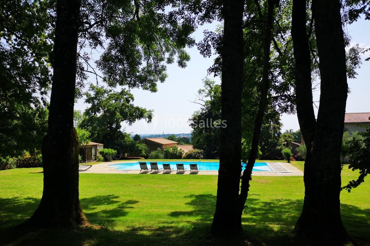 Piscine extérieure entourée de chaises longues, située dans un jardin arboré avec vue dégagée sur l'horizon.