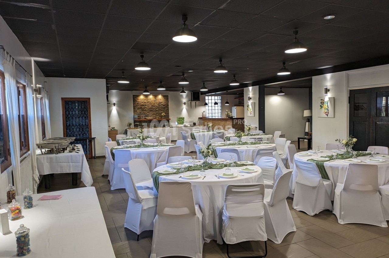 Salle de réception décorée avec des tables rondes dressées, nappes blanches et éclairage suspendu.