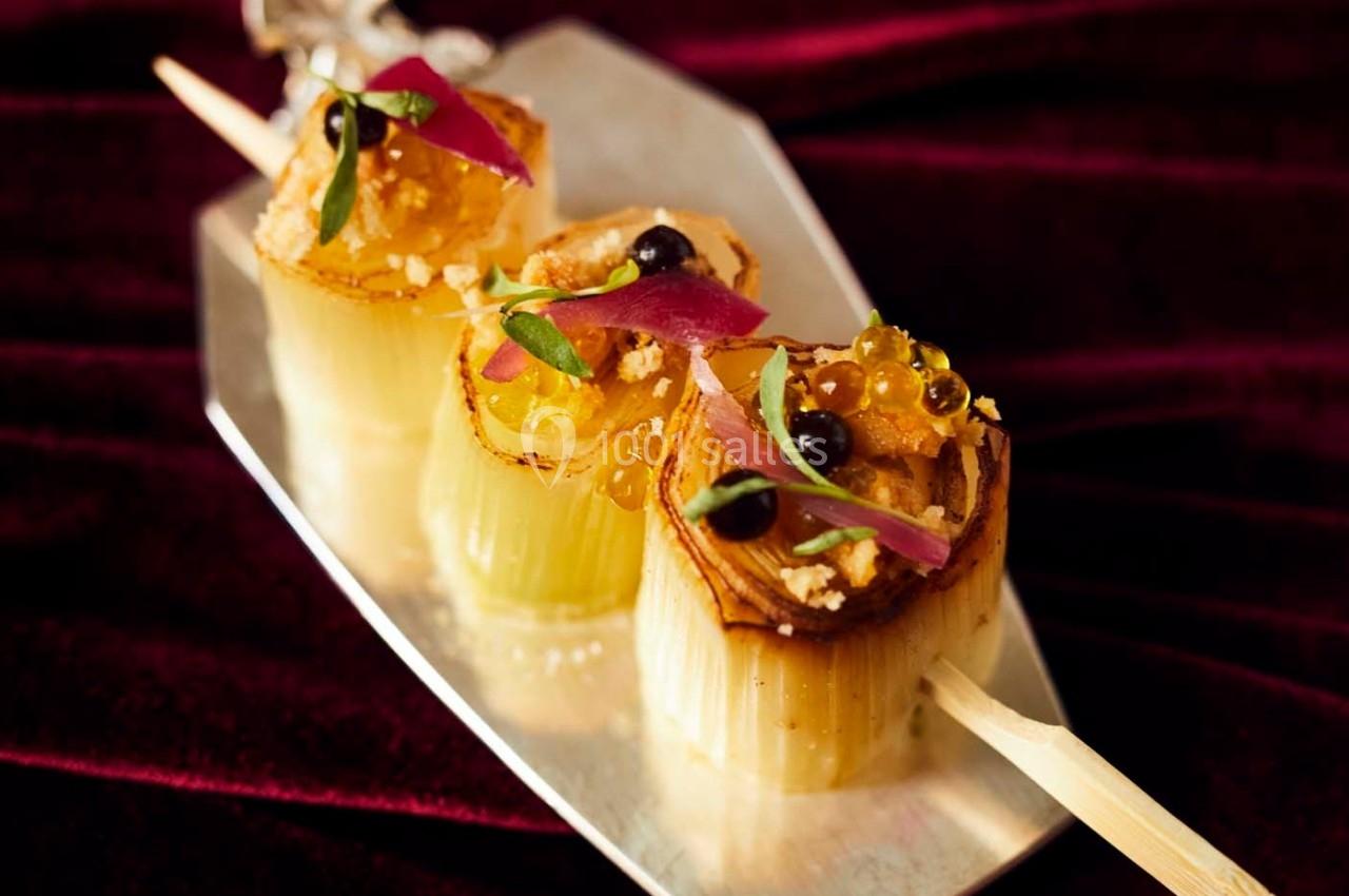 Brochette de poireaux grillés garnis de perles de sauce, herbes fraîches et oignons rouges sur un plateau argenté.