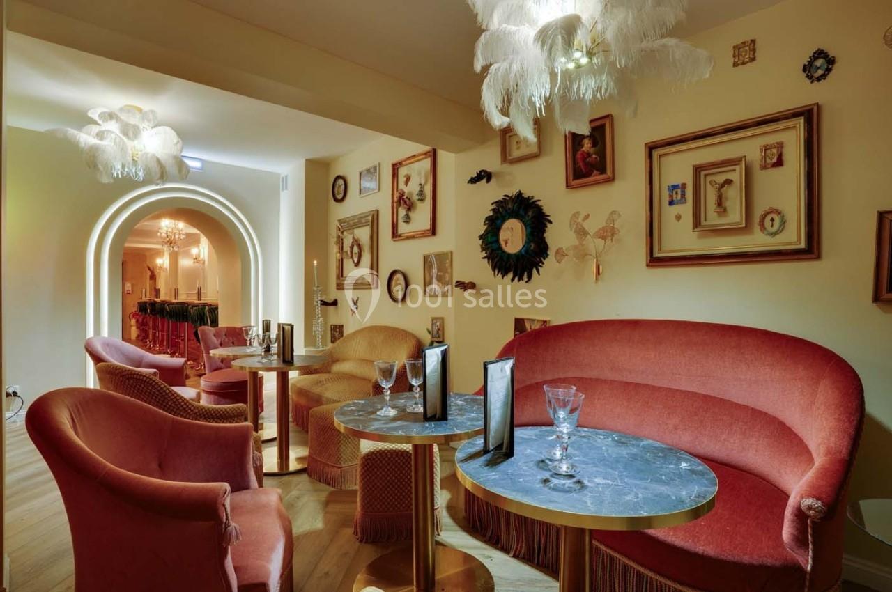 Salon élégant avec fauteuils en velours rouge, tables en marbre, éclairage doux et décorations murales éclectiques.
