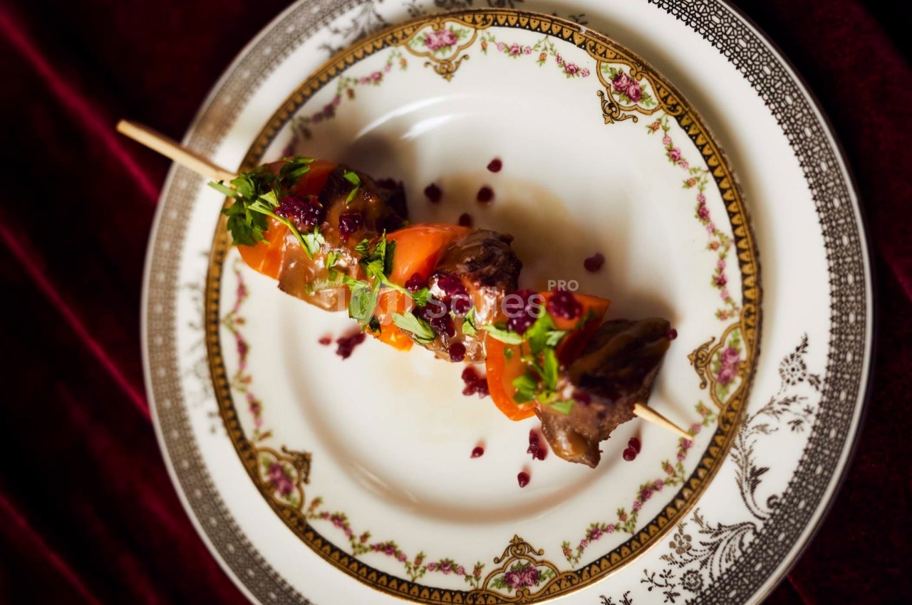 Brochette de viande et légumes garnie de persil et de sauce, servie sur une assiette décorative.