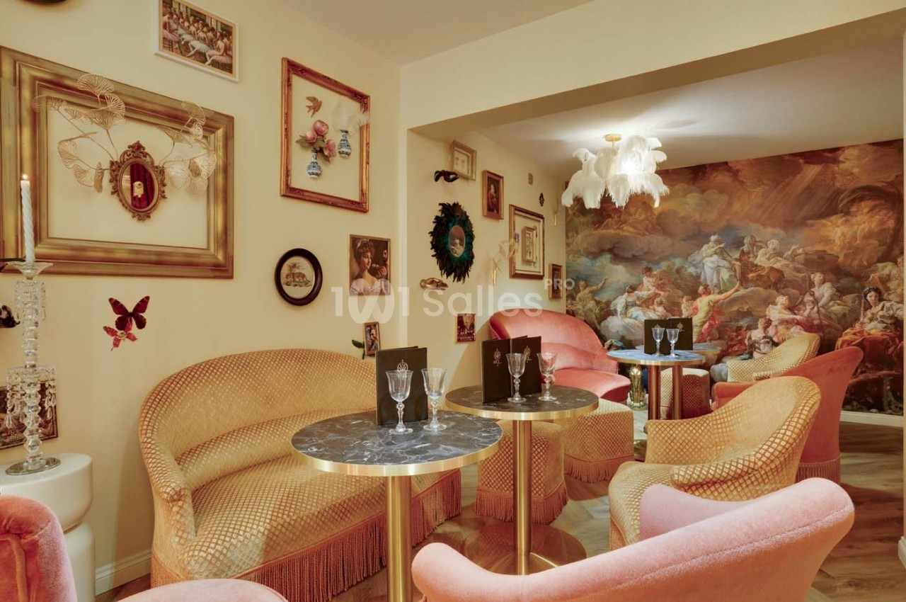 Salon cosy avec fauteuils pastel, tables en marbre, décorations murales éclectiques et fresque murale baroque.