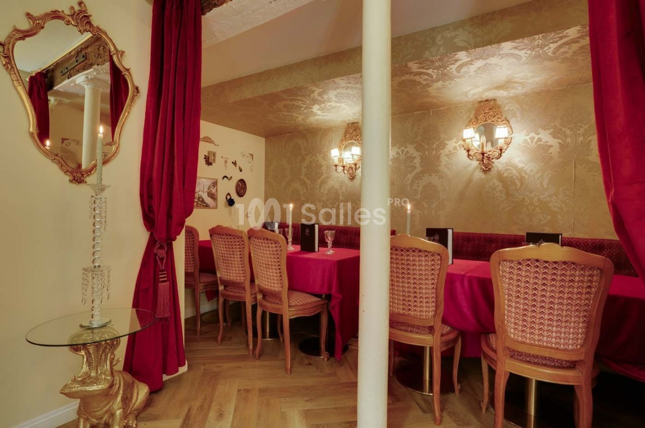 Salle à manger élégante avec table rouge, chaises en bois sculpté, murs ornés et éclairage tamisé.