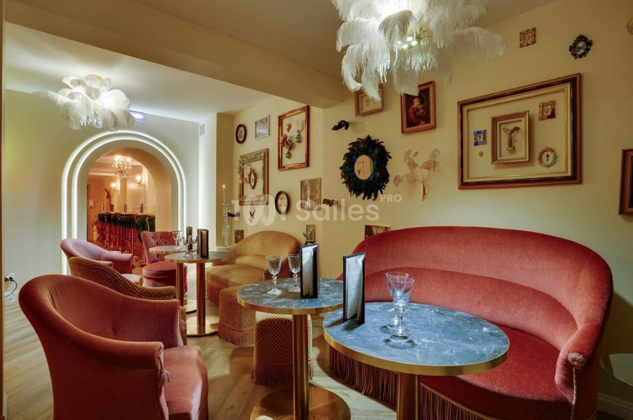 Salon élégant avec fauteuils en velours rouge, tables en marbre, éclairage doux et décorations murales éclectiques.
