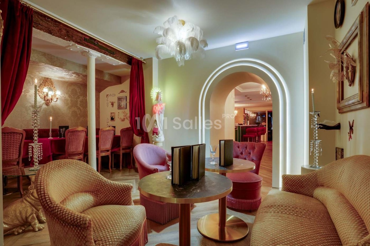 Salon élégant avec fauteuils et tables basses, éclairage tamisé, rideaux rouges et décorations classiques.