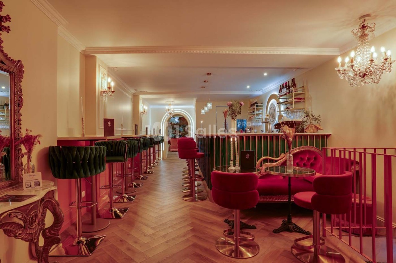 Intérieur d'un bar élégant avec tabourets en velours rouge, comptoir vert et éclairage chaleureux.