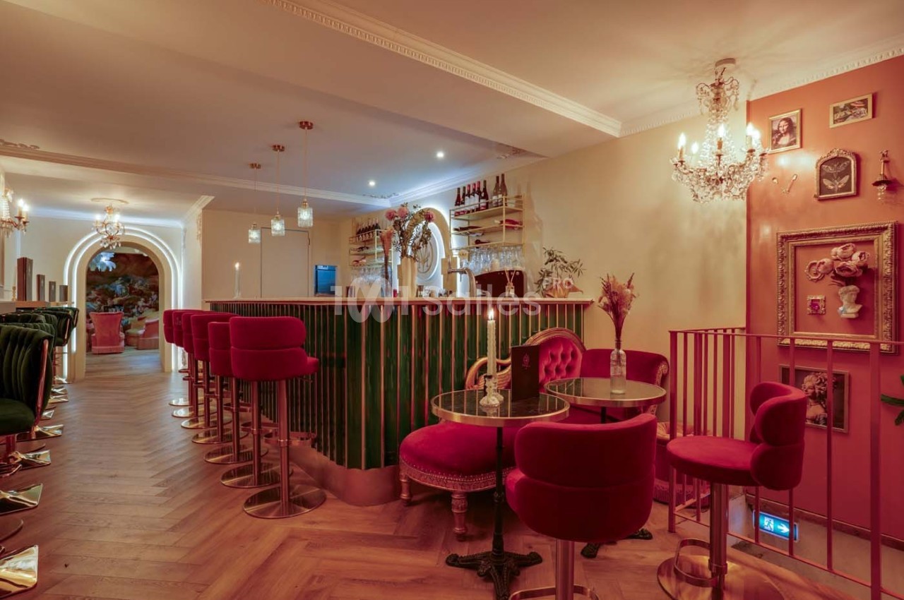 Intérieur d'un bar élégant avec des fauteuils rouges, un comptoir vert, un éclairage chaleureux et une décoration raffinée.
