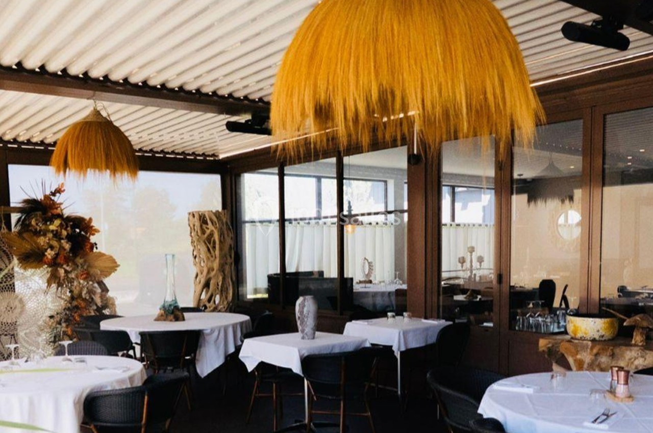 Salle de restaurant lumineuse avec tables dressées, grandes suspensions en fibres naturelles et décoration végétale.