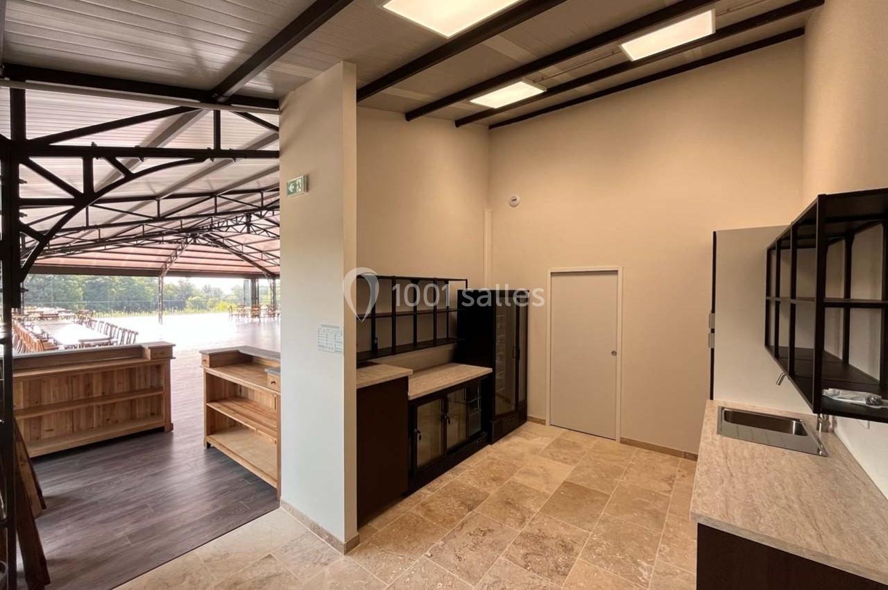 Espace intérieur avec comptoirs en bois et métal, sol en pierre, éclairage au plafond et vue sur une terrasse extérieure.