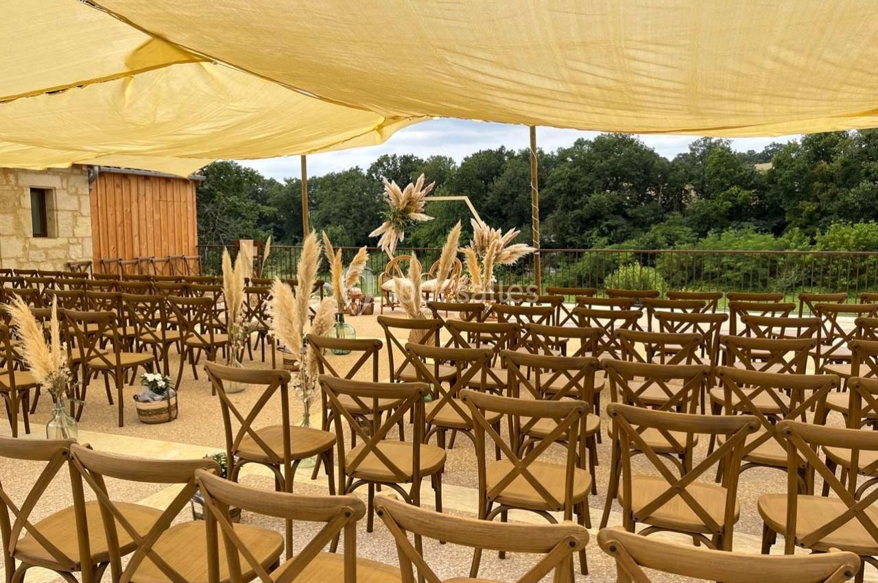 Chaises en bois disposées en rangées sous une toile beige, avec des décorations en herbe de la pampa, en extérieur.