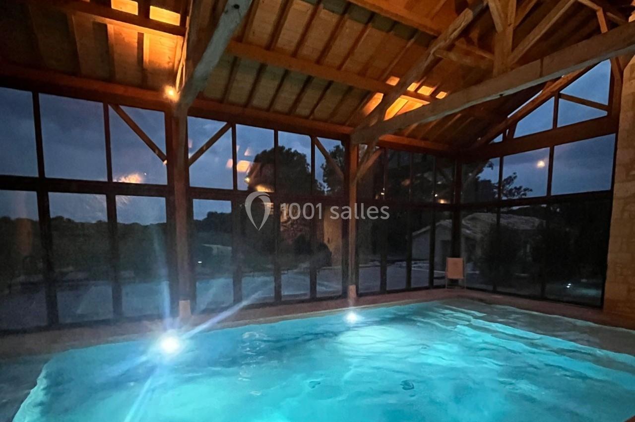 Piscine intérieure éclairée la nuit, entourée de grandes baies vitrées et d'une structure en bois.
