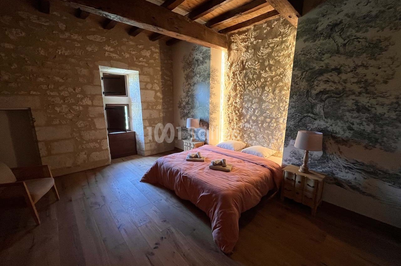 Chambre avec lit double, murs en pierre, poutres apparentes et éclairage doux, décorée de motifs muraux naturels.