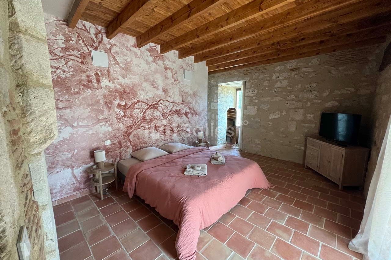 Chambre avec murs en pierre, plafond en bois, lit double avec couverture rose et sol en carrelage.