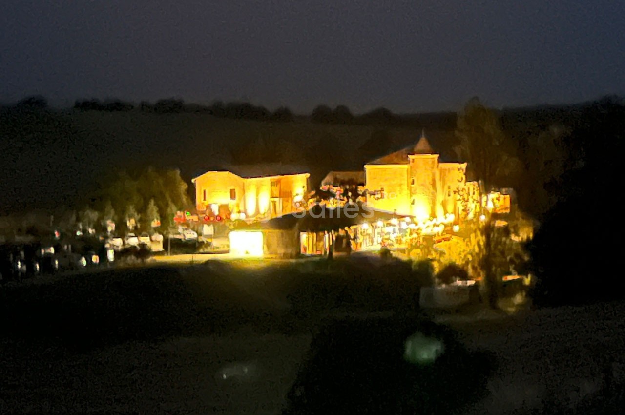 Bâtiments éclairés de nuit dans un paysage rural sombre, entourés de végétation et de quelques structures.