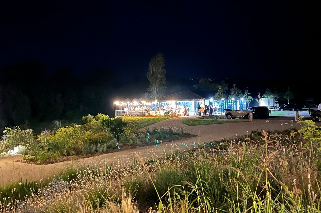 Vue nocturne d'un bâtiment éclairé entouré de végétation et d'un parking, dans un cadre naturel.