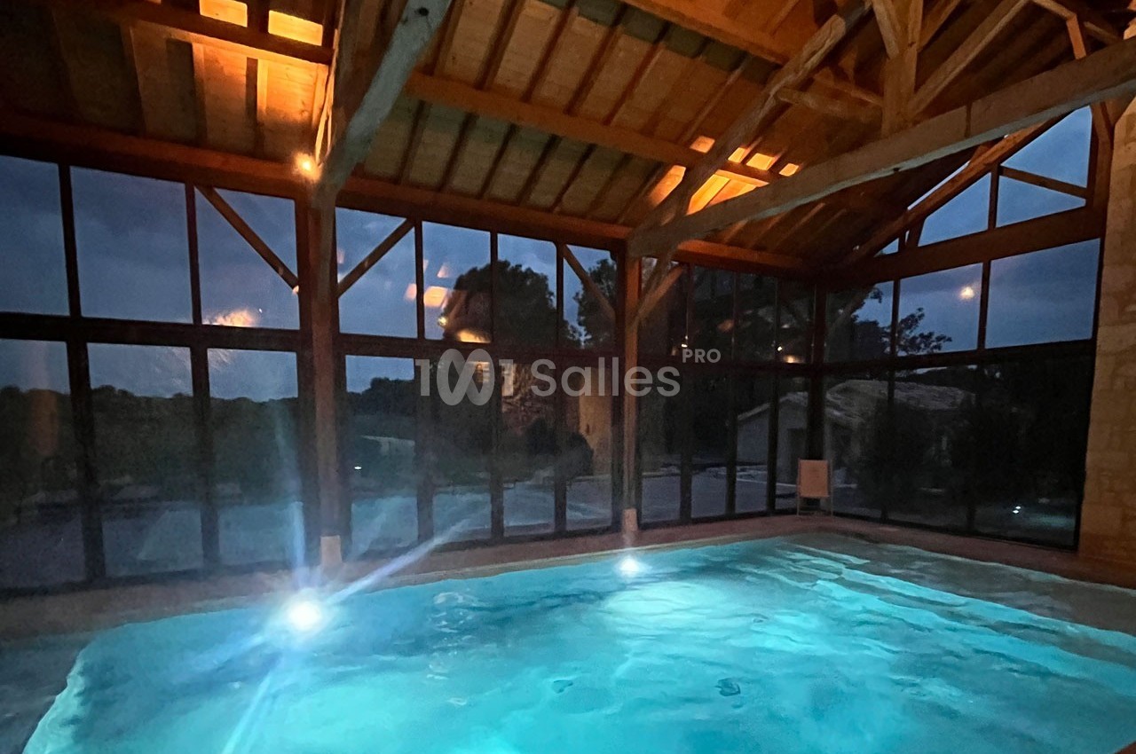 Piscine intérieure éclairée la nuit, entourée de grandes baies vitrées et d'une structure en bois.