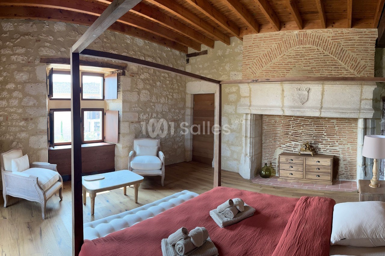 Chambre avec lit à baldaquin, cheminée en pierre, plafond en bois et mobilier élégant dans un décor rustique.