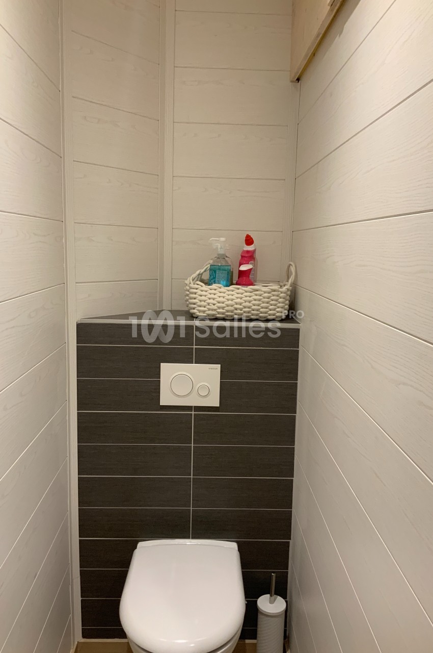 Toilettes modernes avec murs en bois clair, étagère intégrée contenant des produits ménagers dans un panier tressé.