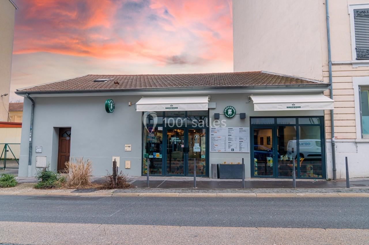 Façade d'un café avec deux grandes vitrines, enseignes et menu affiché, sous un ciel coloré au coucher du soleil.