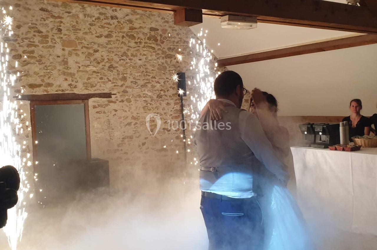Un couple danse dans une salle en pierre, entouré de fumée et d'étincelles, sous le regard de quelques invités.