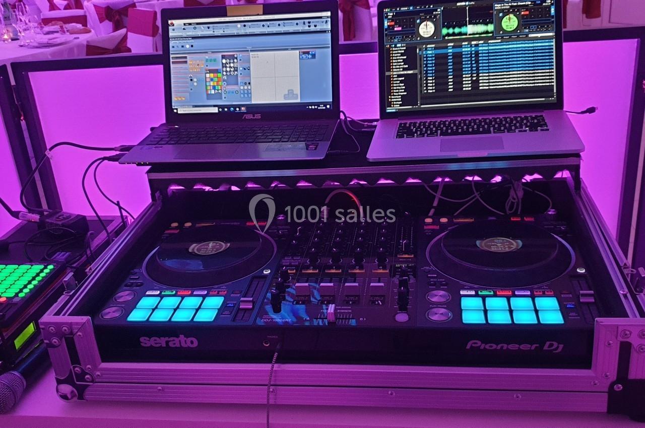 Équipement de DJ avec platines, table de mixage, deux ordinateurs portables et éclairage violet en arrière-plan.