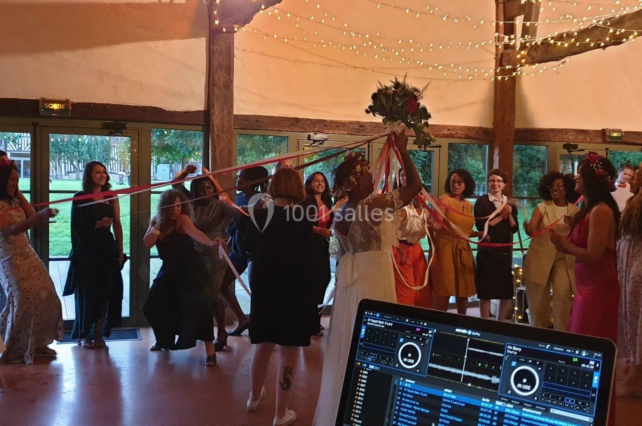 Des invités dansent autour de la mariée tenant des rubans colorés sous des guirlandes lumineuses dans une salle festive.