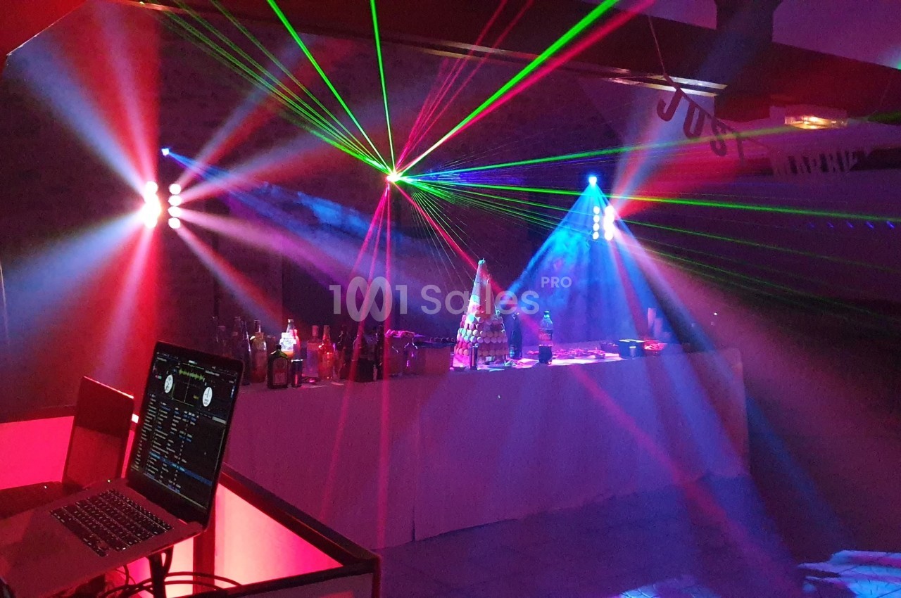 Jeu de lumières colorées et lasers éclairant une salle avec une table de mixage et un ordinateur portable.