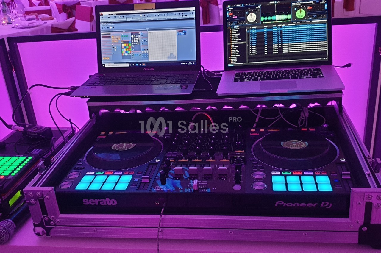 Équipement de DJ avec platines, table de mixage, deux ordinateurs portables et éclairage violet en arrière-plan.
