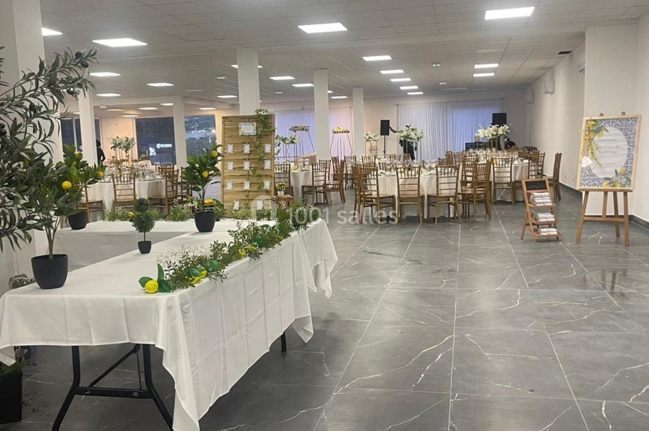 Salle de réception lumineuse avec tables décorées, plantes en pot et présentoir en bois au premier plan.