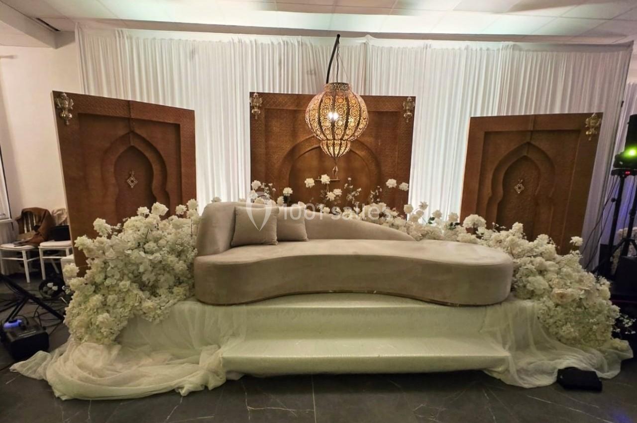 Canapé beige entouré de fleurs blanches, devant des panneaux décoratifs en bois et un luminaire suspendu.
