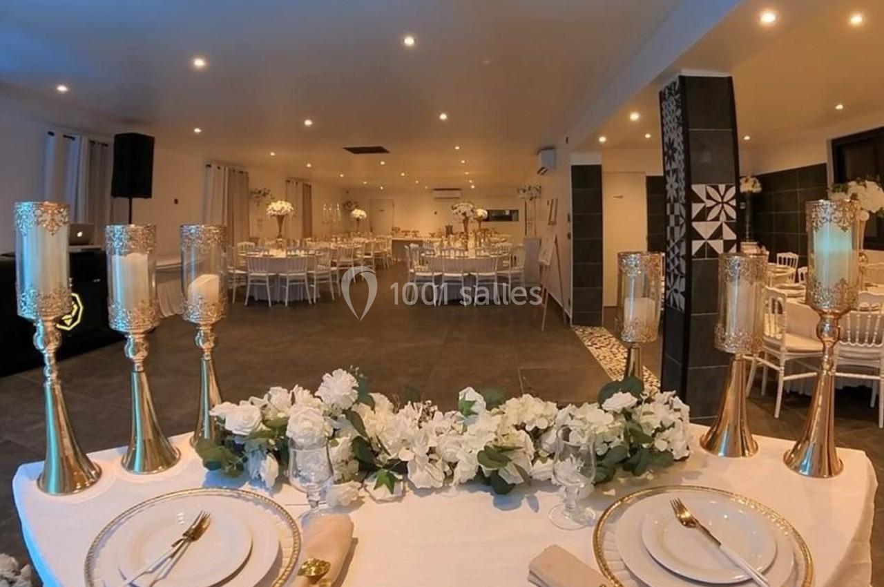 Salle de réception élégamment décorée avec des chandeliers dorés, des fleurs blanches et des tables dressées.