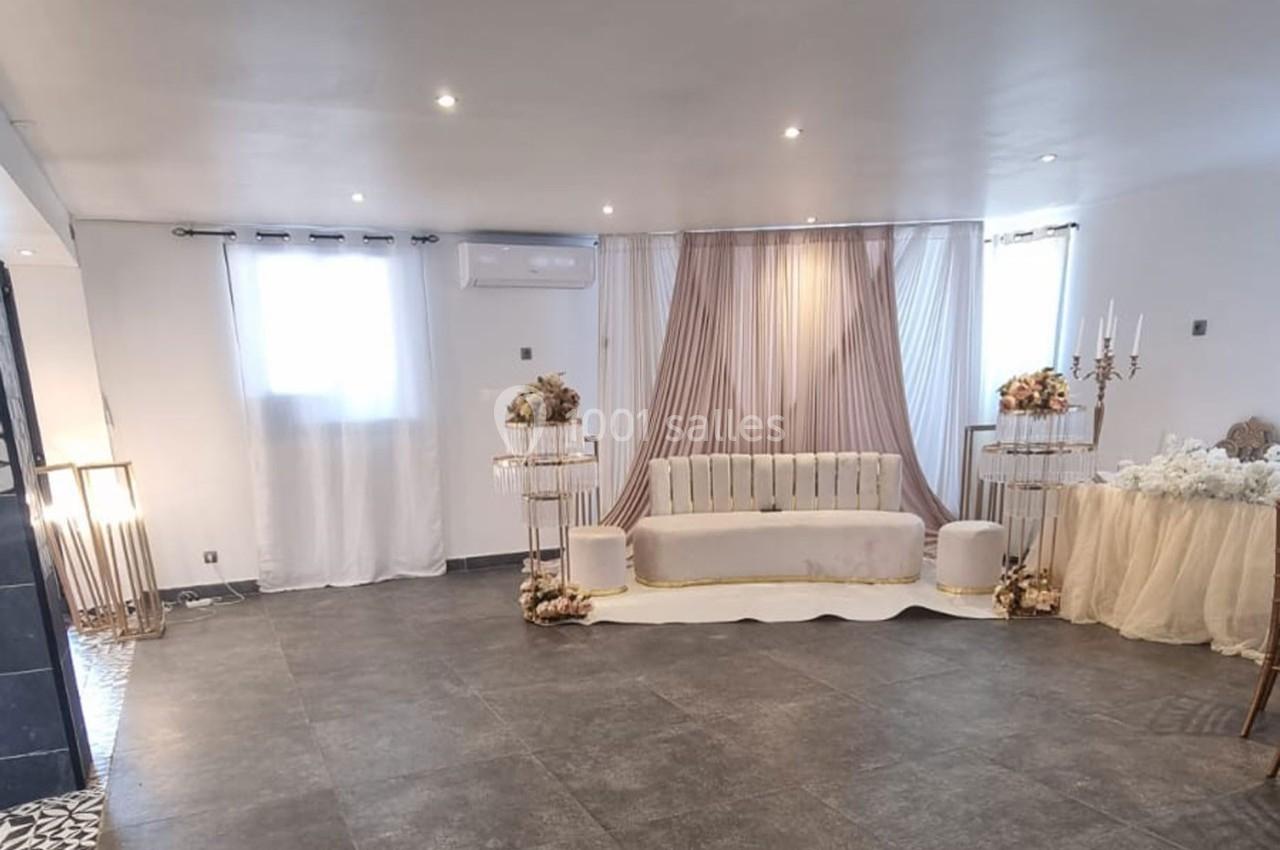 Salle décorée avec un canapé beige, rideaux roses, tables ornées de fleurs et chandeliers, éclairage tamisé.