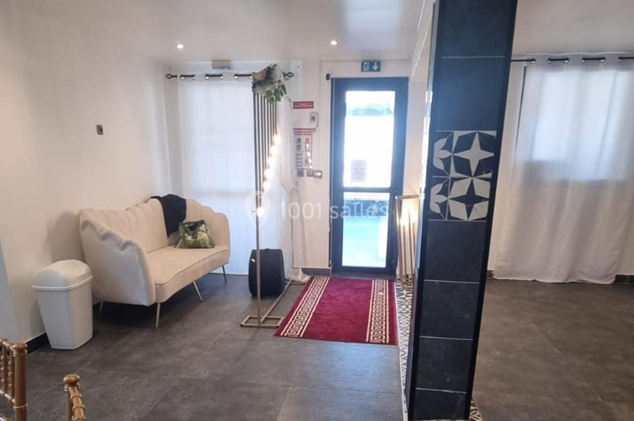 Hall d'entrée lumineux avec canapé blanc, tapis rouge, lampadaire et porte vitrée donnant sur l'extérieur.