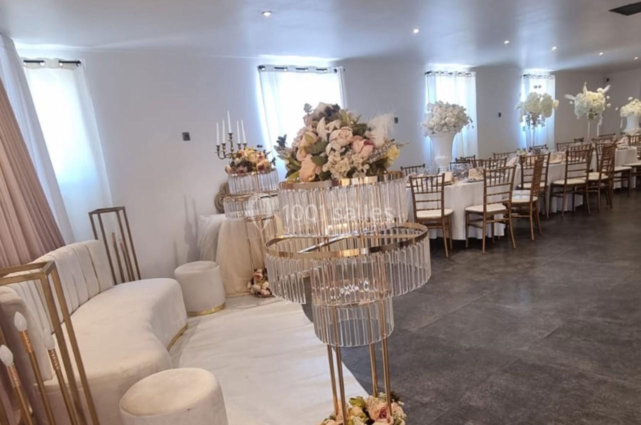 Salle de réception décorée avec des fleurs, des chaises dorées et des tables dressées pour un événement.