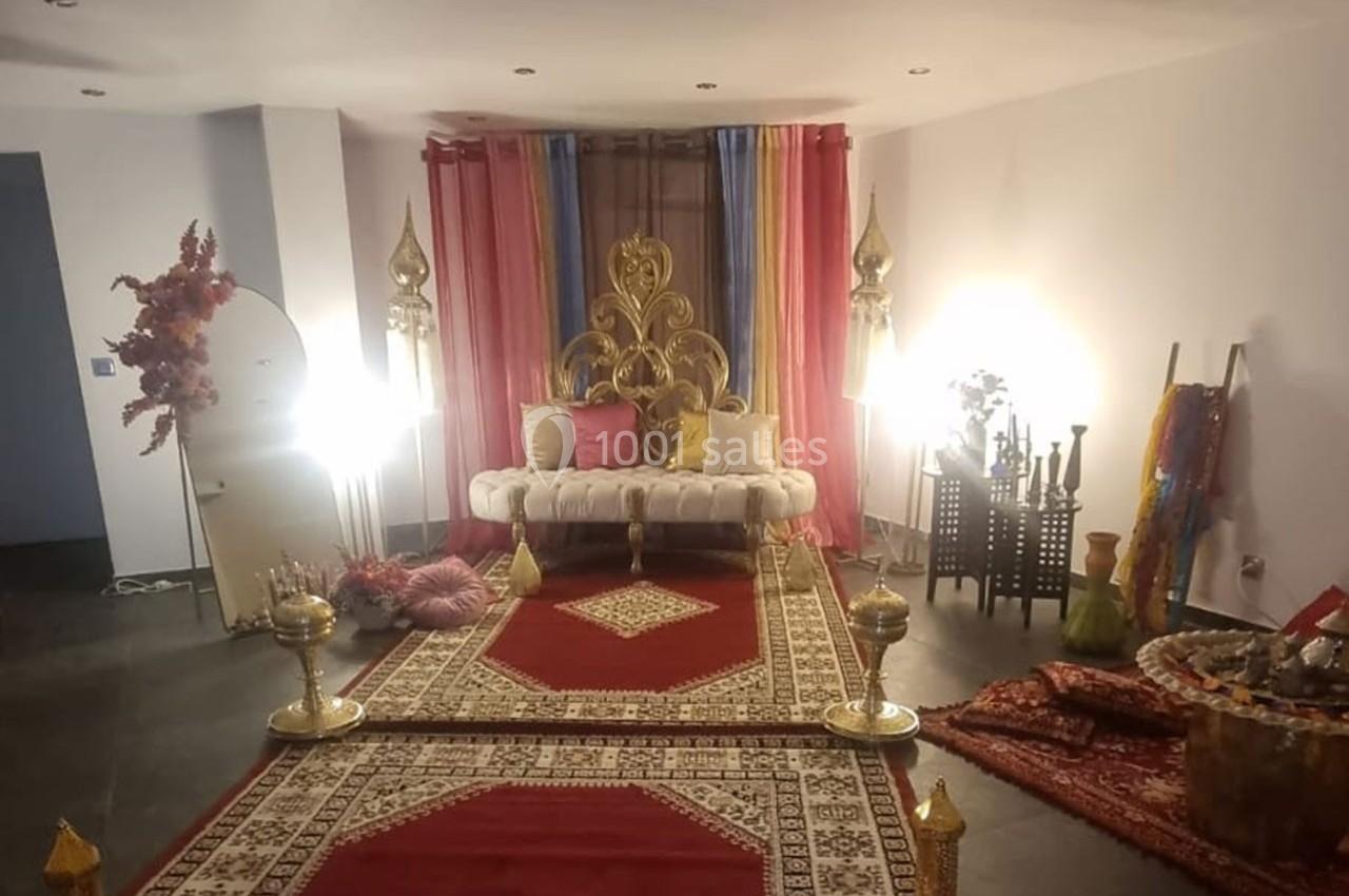 Décoration intérieure avec canapé doré, tapis rouges, rideaux colorés et accessoires orientaux dans une pièce éclairée.