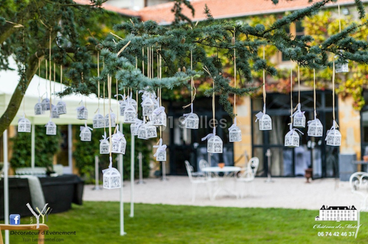 Des petites lanternes blanches suspendues à un arbre décorent un espace extérieur devant un bâtiment.