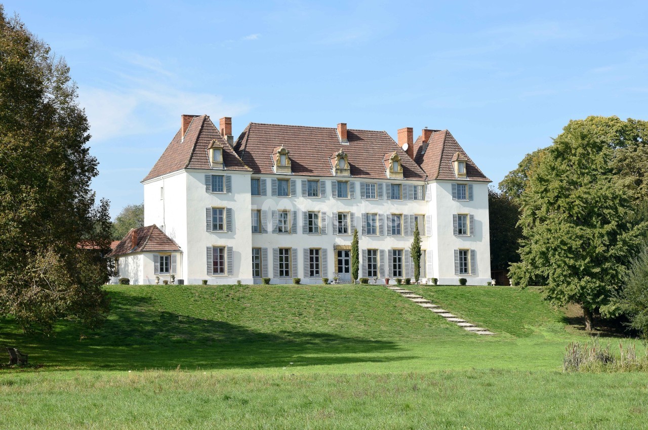 Grande maison blanche à plusieurs étages avec des volets colorés, située sur une pelouse verdoyante par temps clair.