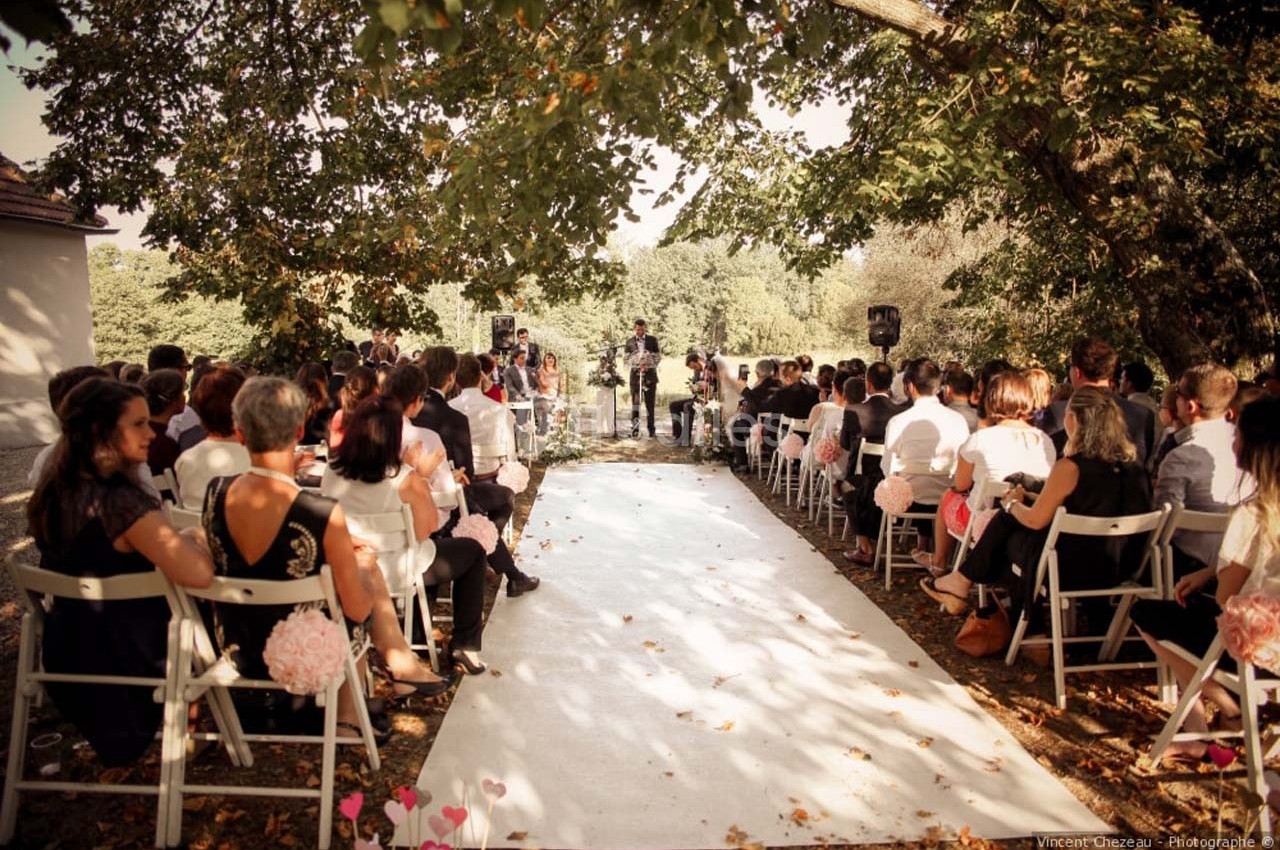 Cérémonie de mariage en plein air avec des invités assis sous des arbres, face à un officiant.