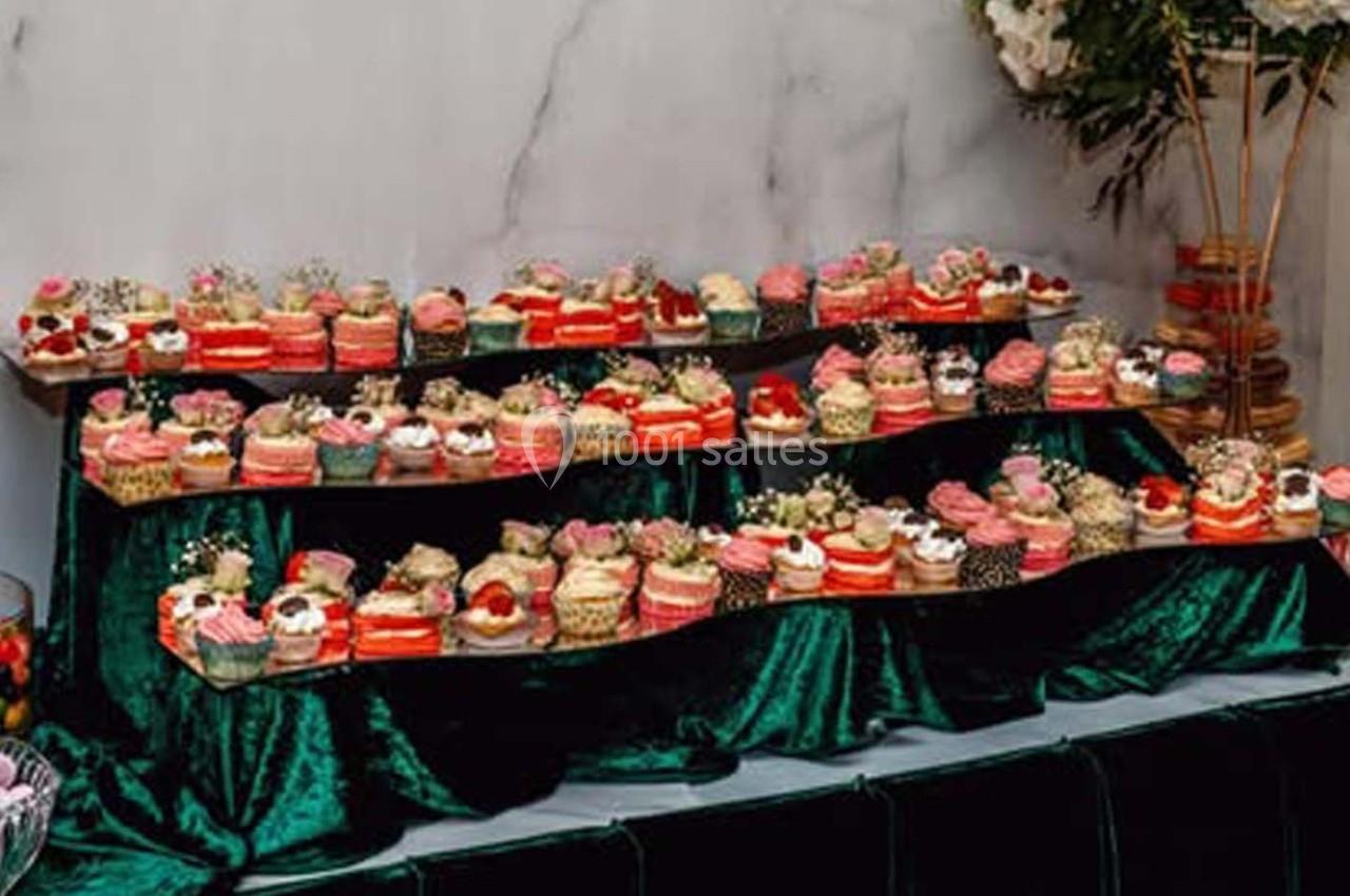 Présentation de desserts variés, notamment des cupcakes et gâteaux, disposés sur des étagères recouvertes de tissu vert.