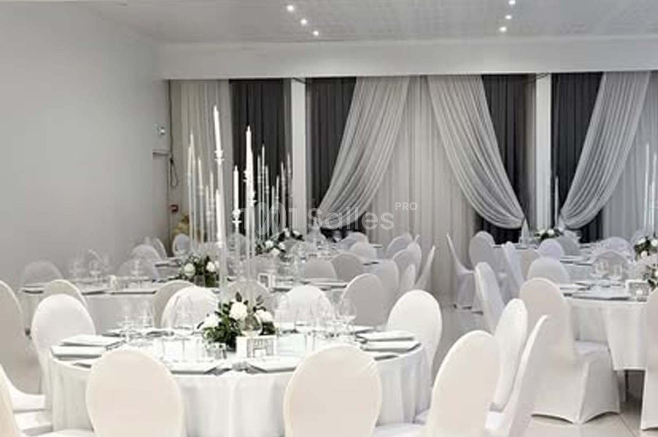 Salle de réception élégante avec tables rondes décorées de nappes blanches, chandeliers et arrangements floraux.
