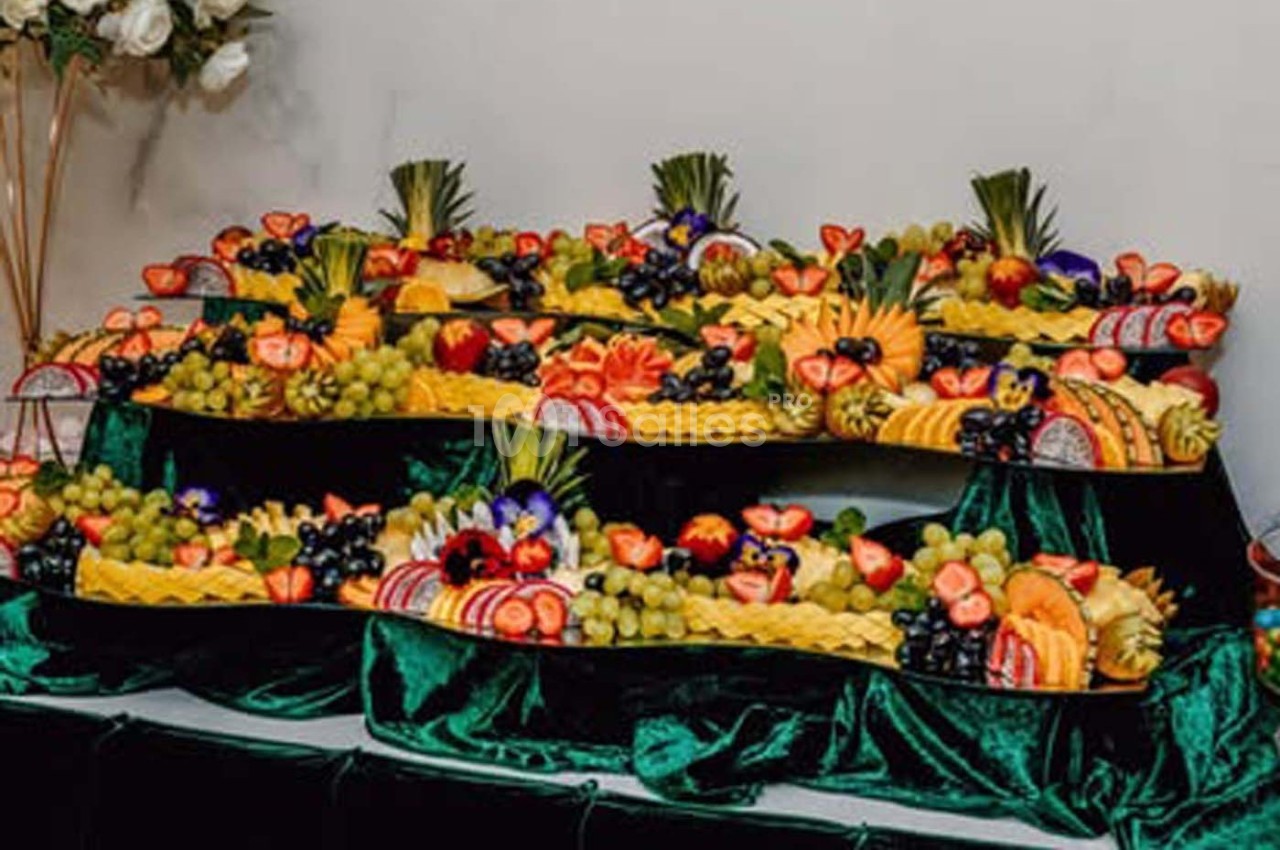 Plateaux garnis de fruits variés, dont ananas, fraises, raisins et agrumes, disposés sur une nappe verte.