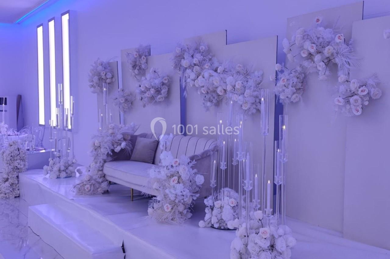 Décor de mariage élégant avec canapé beige, fleurs blanches et chandeliers en verre dans une ambiance lumineuse.