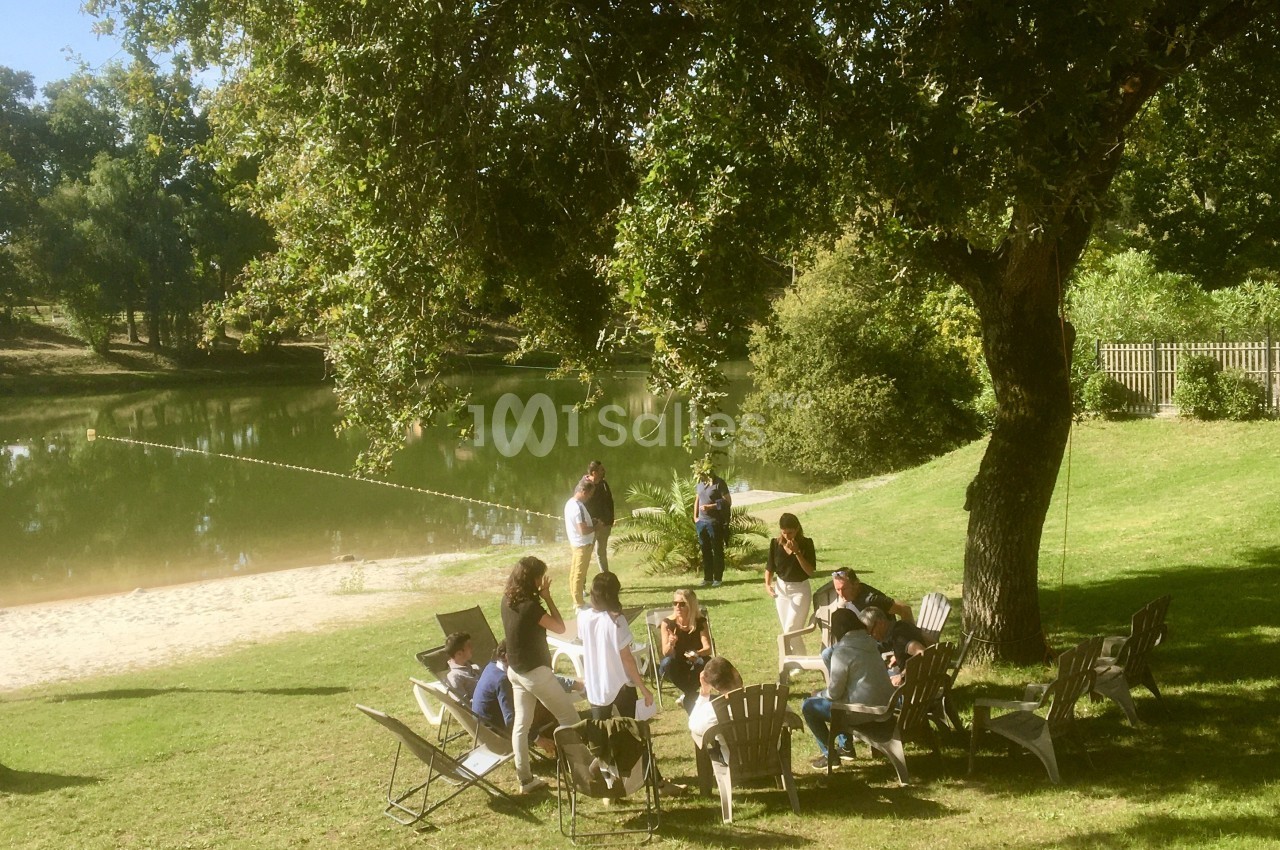 Un groupe de personnes assises sur des chaises en plein air près d'un lac entouré de verdure.