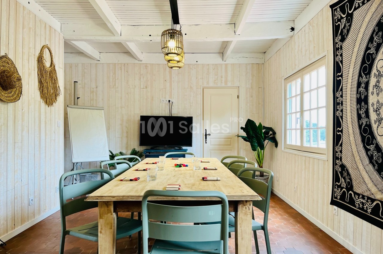 Salle de réunion lumineuse avec table en bois, chaises vertes, tableau de présentation et décoration murale.