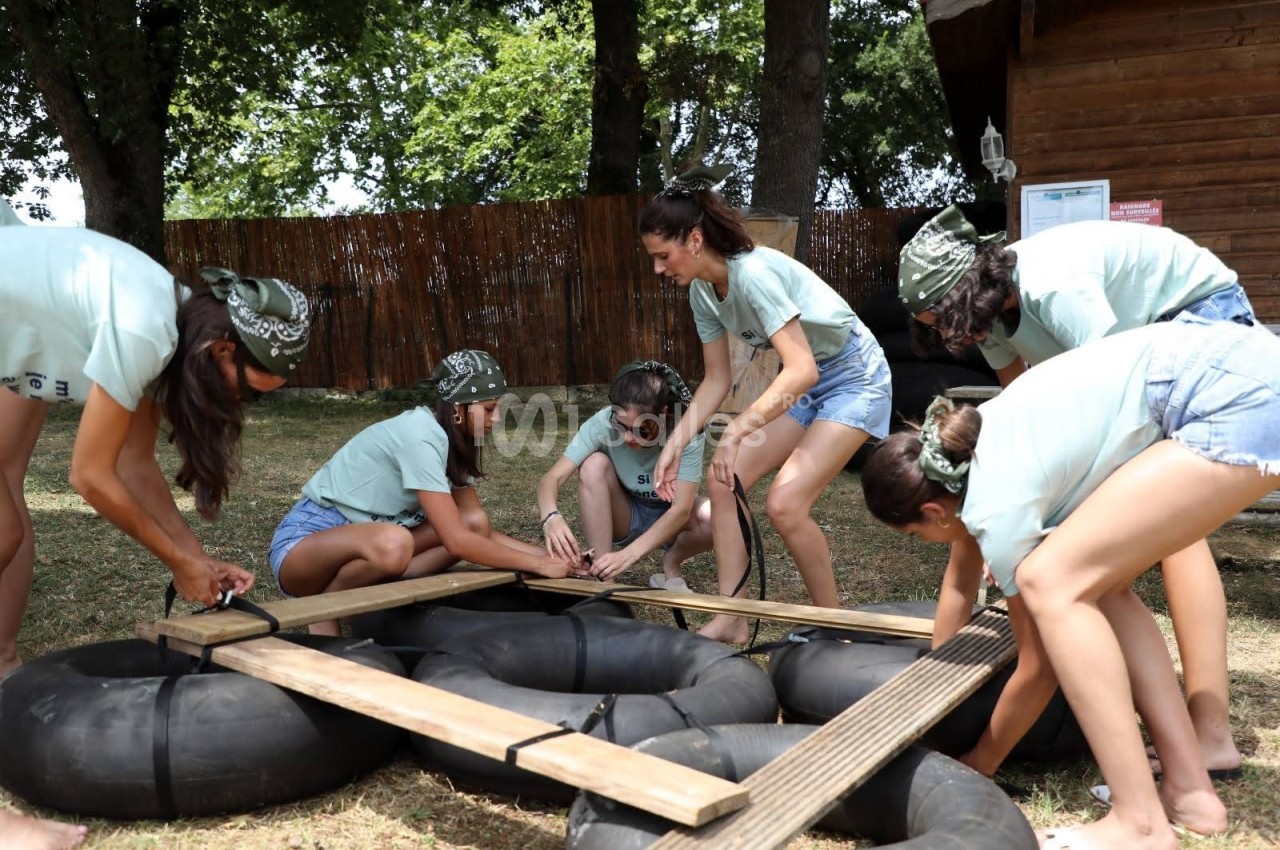 Des jeunes construisent un radeau avec des planches et des chambres à air dans un espace extérieur ombragé.