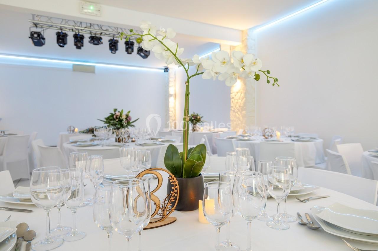 Salle de réception élégante avec tables dressées, centre de table floral et éclairage moderne.