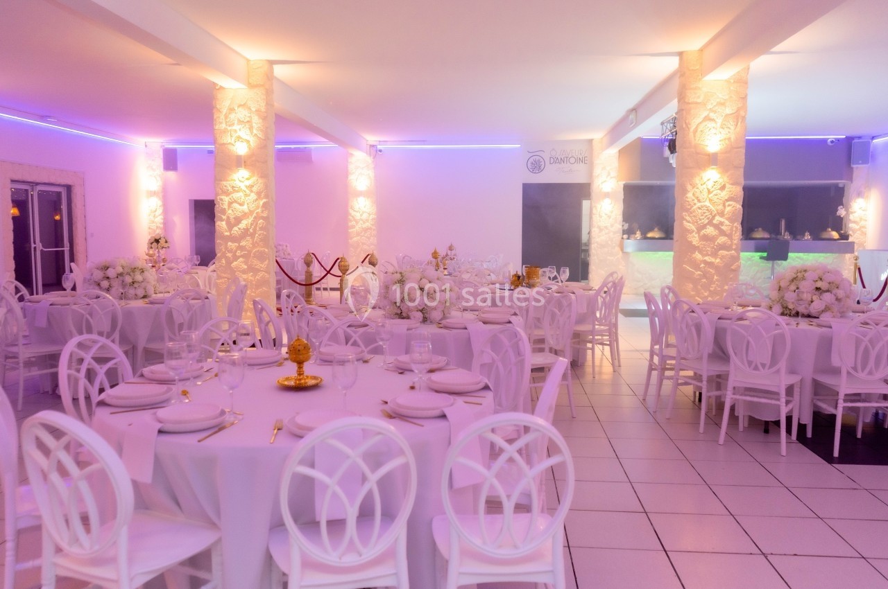 Salle de réception élégante avec tables rondes dressées, chaises blanches et éclairage tamisé violet.