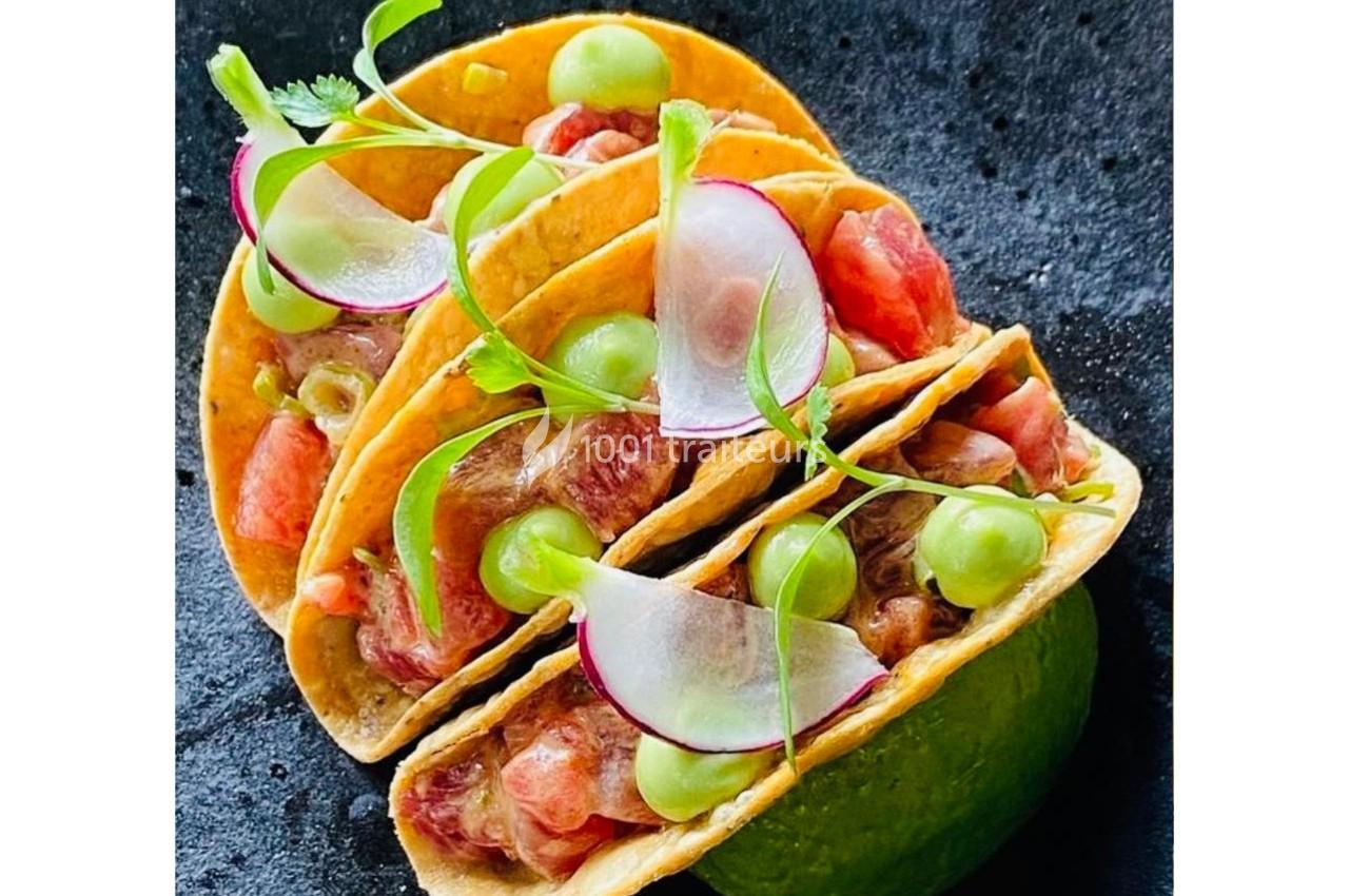 Trois tacos garnis de poisson cru, radis, coriandre et crème verte, présentés sur une surface noire.